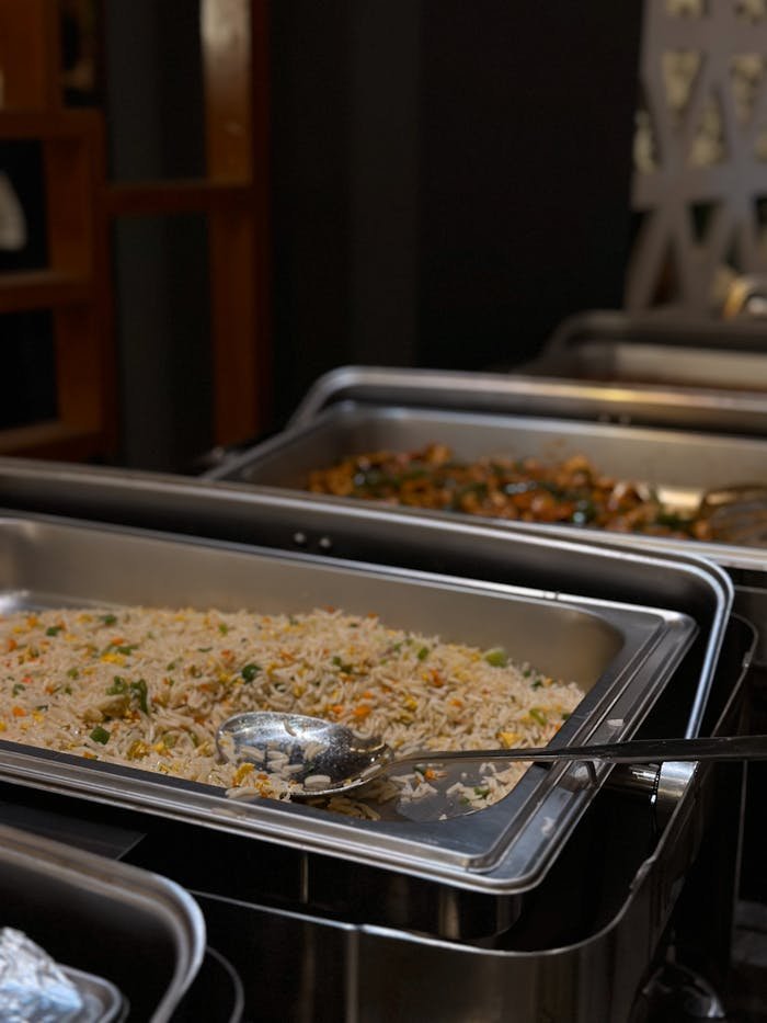A close-up of buffet-style rice and vegetables served in catering trays, ready for guests.