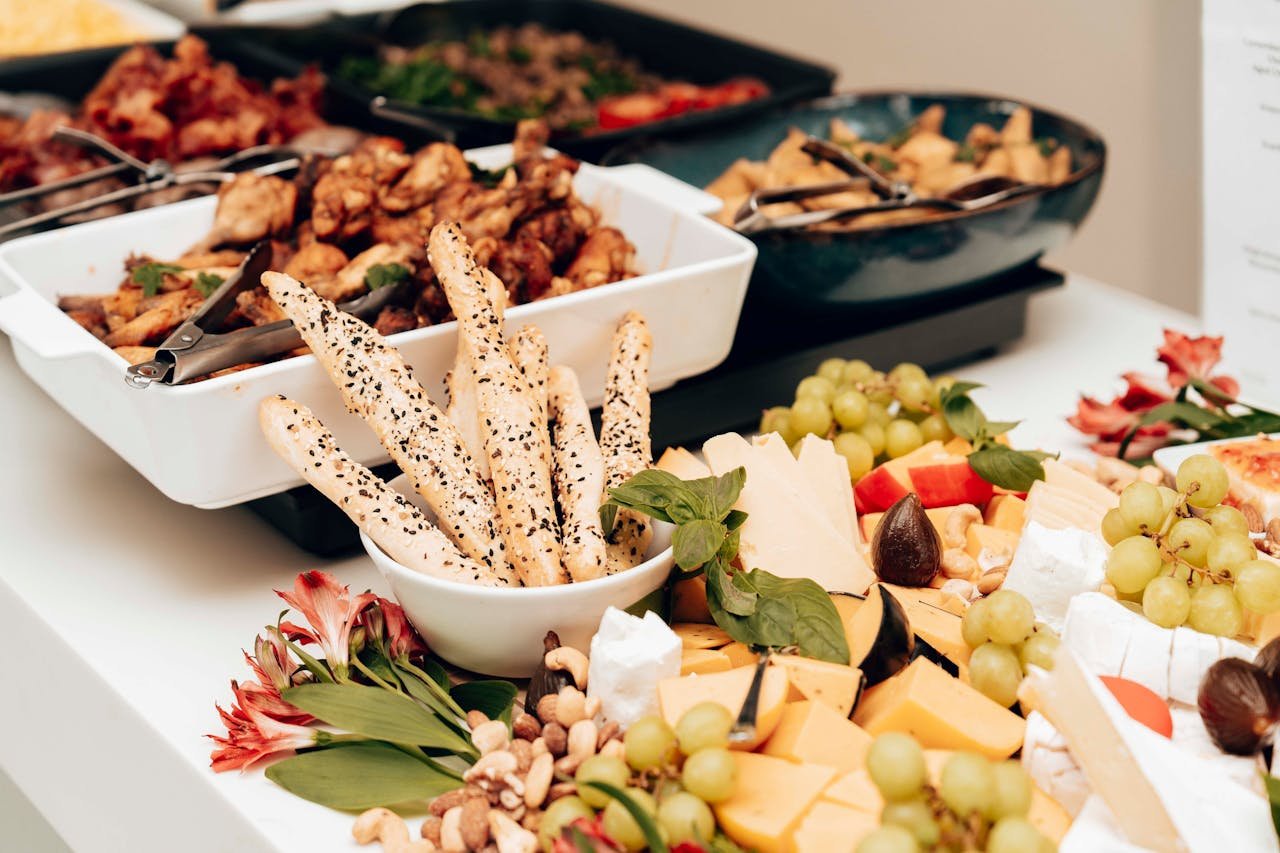 A mouth-watering assortment of cheeses, breadsticks, and fruits in a buffet setting. Perfect for catering events.